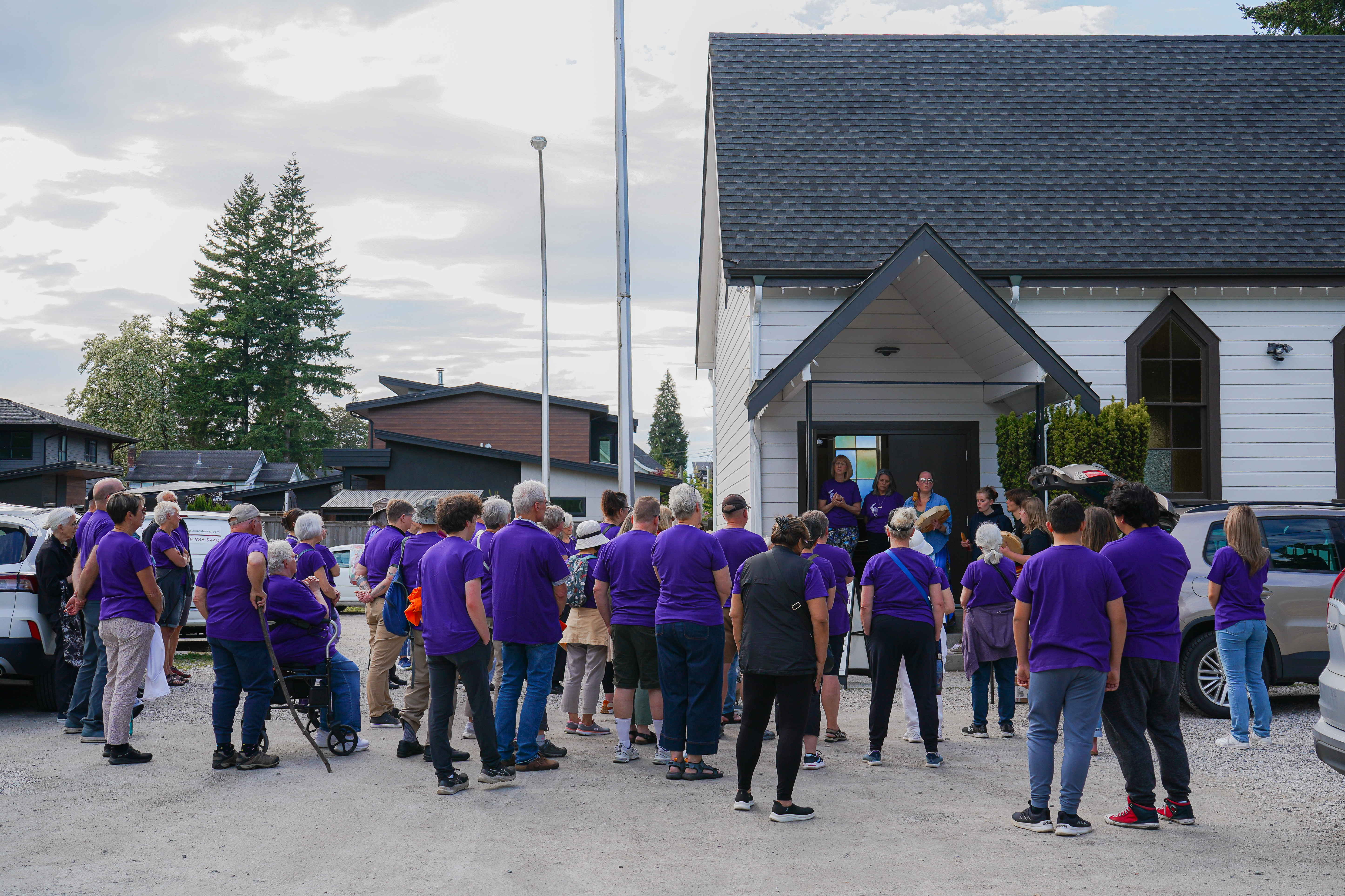 A large group of people wearing purple t-shirts meet outside of a small church