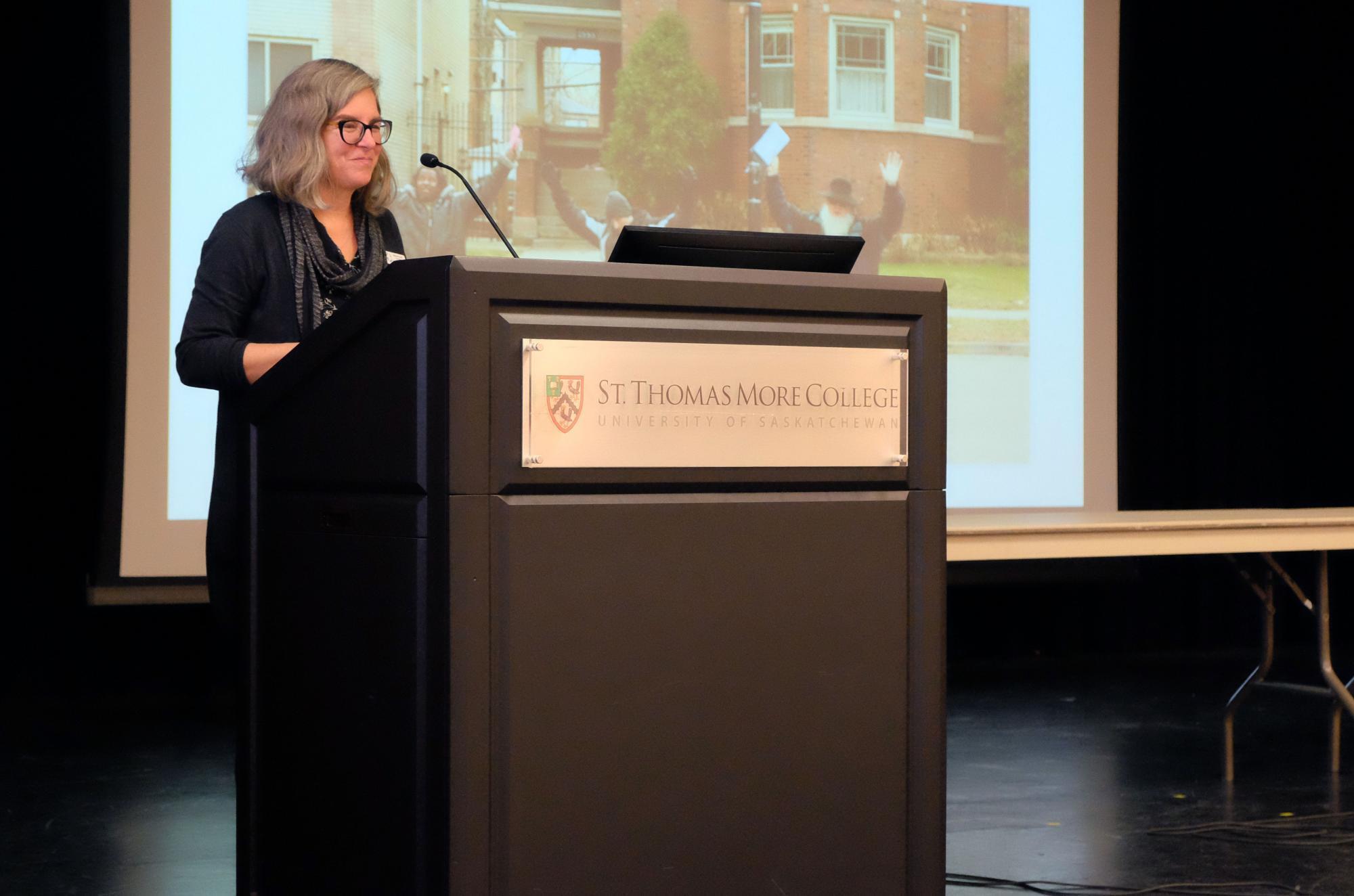 A woman with grey hair speaks in front of a lectern 