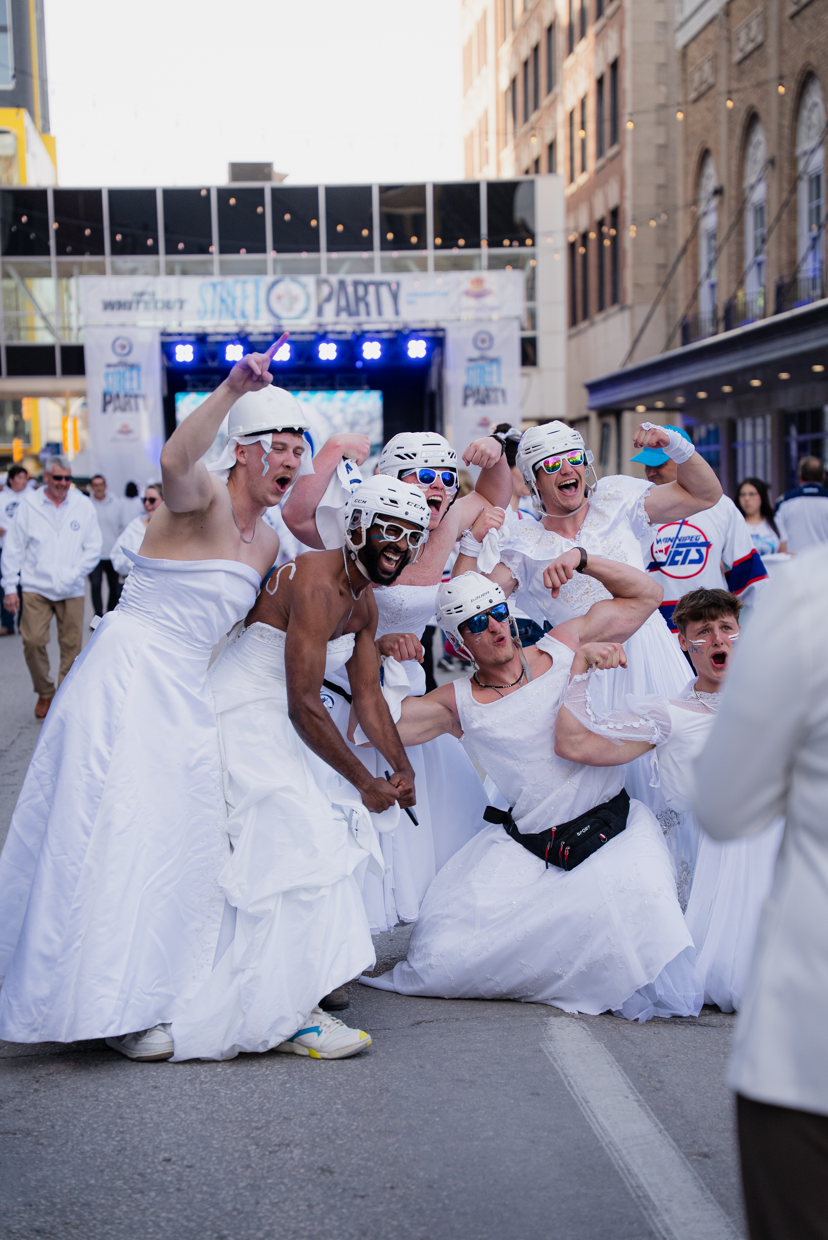 Six men posing in white wedding dresses on a street in downtown Winnipeg.