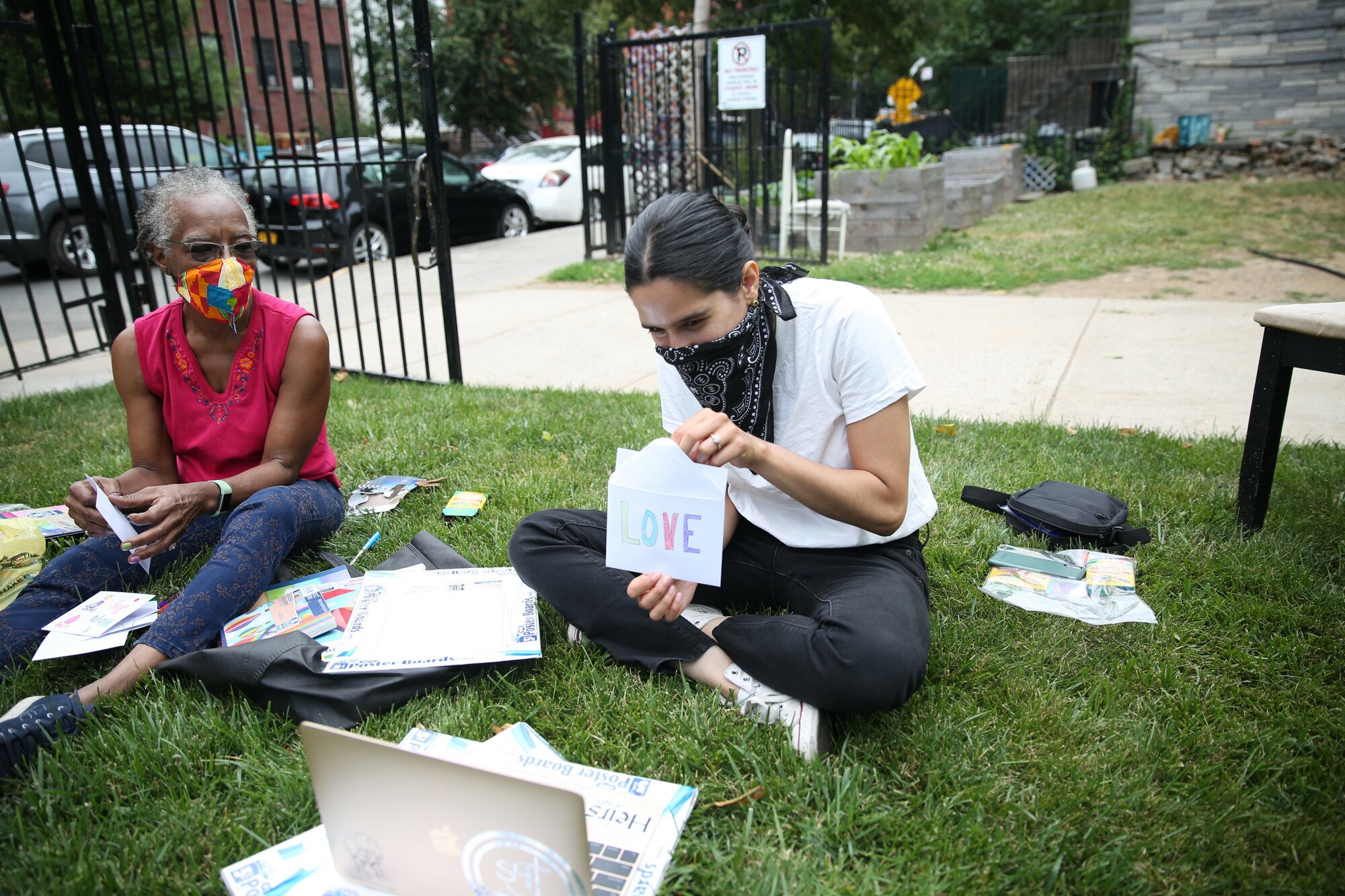 Two women watching a laptop screen while opening an envelope.