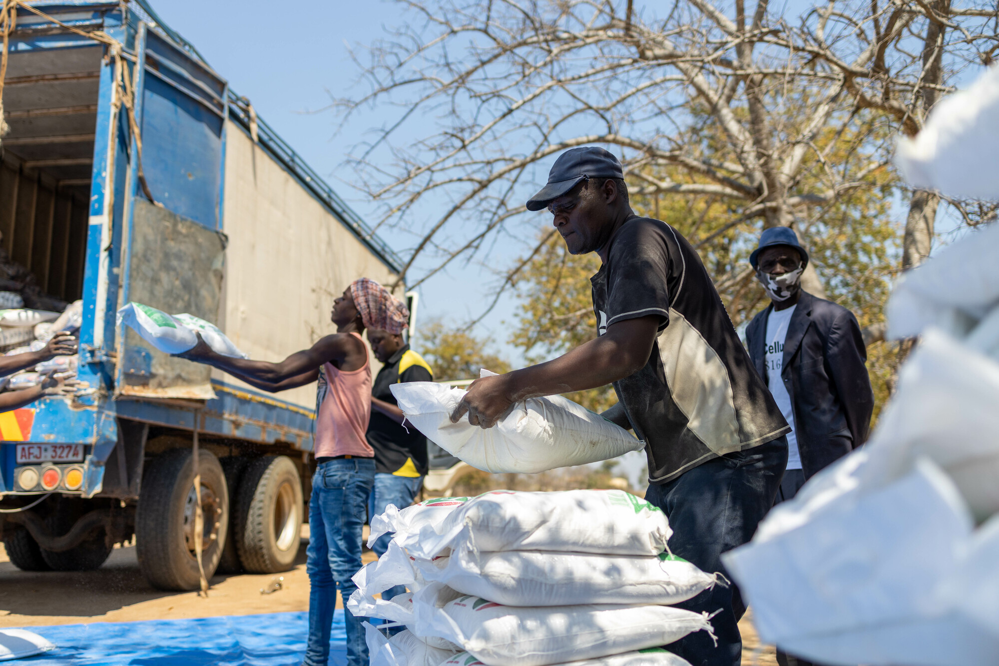 People in Africa unloading large white bags from a truck.
