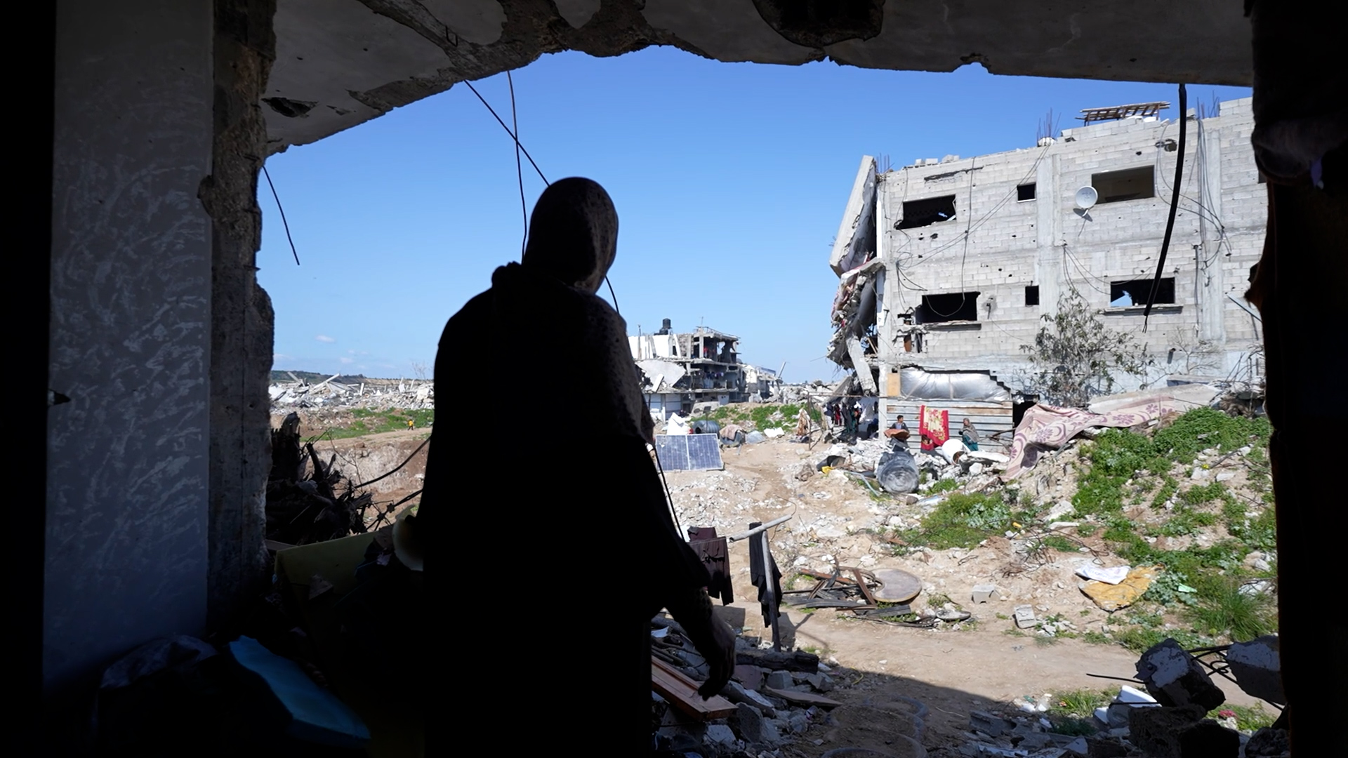 woman with back to camera looking through a space where a wall used to be at the broken building, rubble around her at rubble