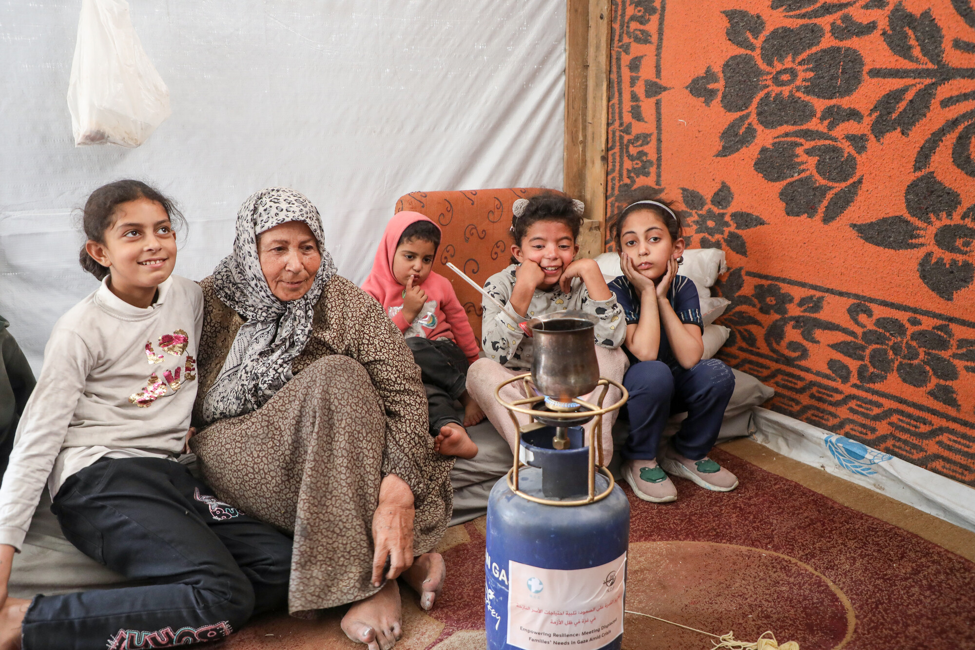 woman and children sitting on floor behind portable gas stove