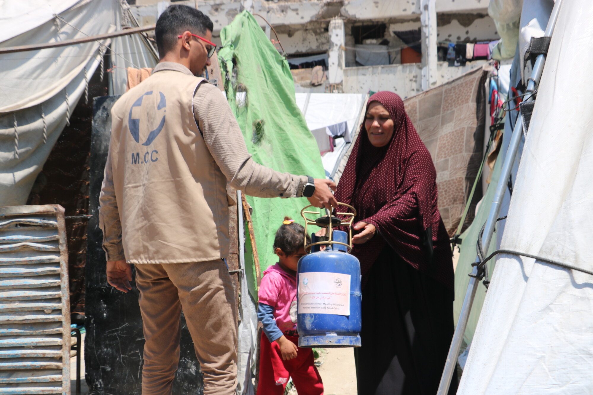 man hands portable gas stove to woman standing outside tent