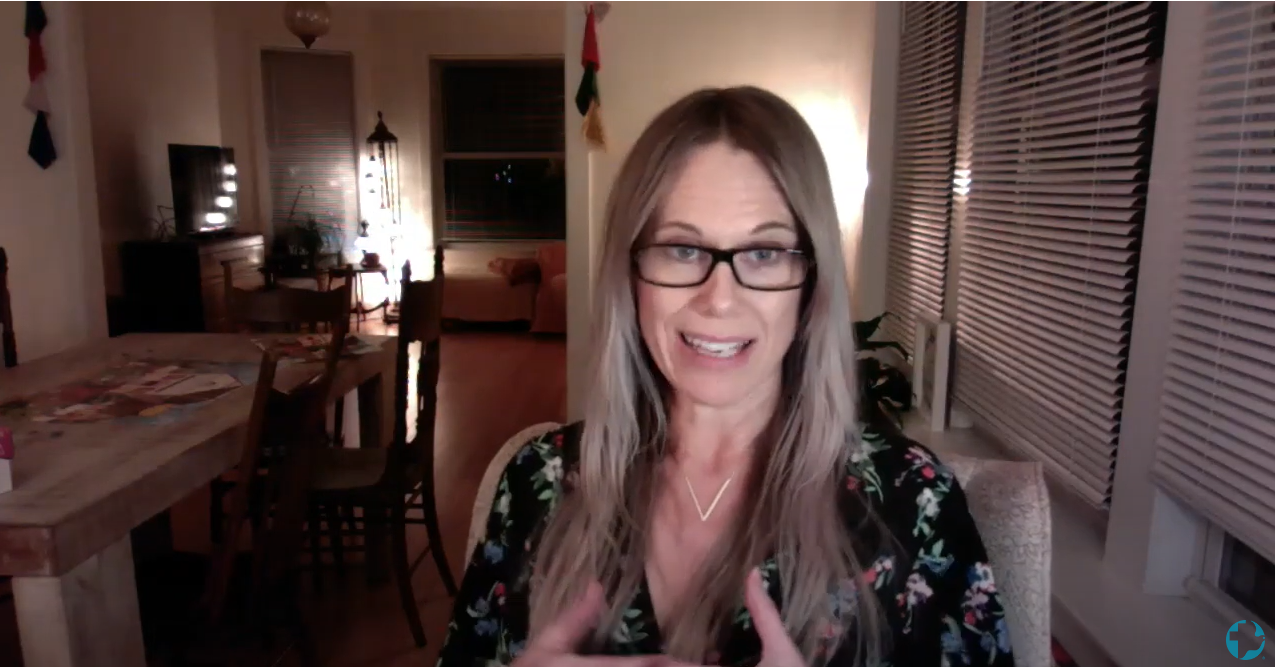 A woman with long hair and glasses speaks into the camera during a video call
