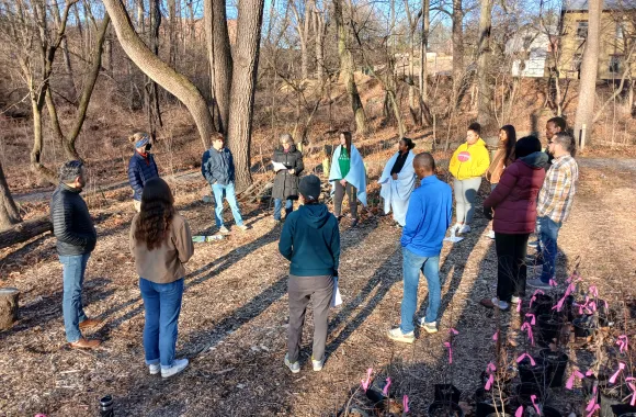 A group of young adults stand in a circle in the woods of Akron.
