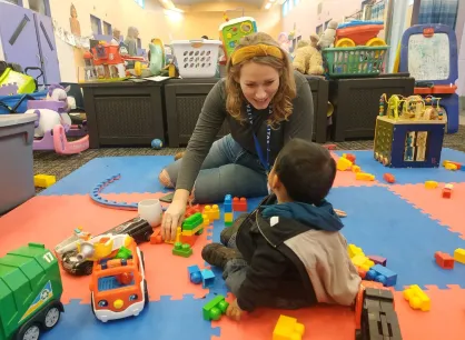 A smiling person sits on the floor with a small child.