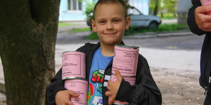 A boy* holds cans of meat he and his mother (not pictured) received from volunteers with MCC partner Association of Mennonite Brethren Churches of Ukraine (AMBCU). The canned meat was part of a distri