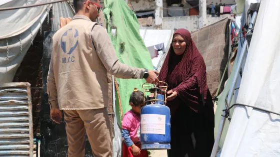man hands portable gas stove to woman standing outside tent