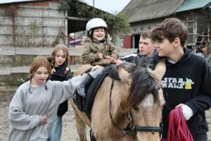Three-year-old Vasylisa* sits calmly with assistance from volunteers during therapeutic horse riding for children who are displaced and affected by war.MCC, with partner Association of Mennonite B