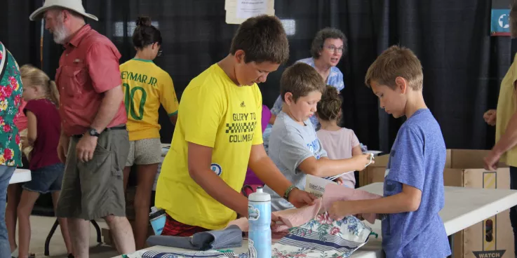three boys stand around table packing hyiene kits